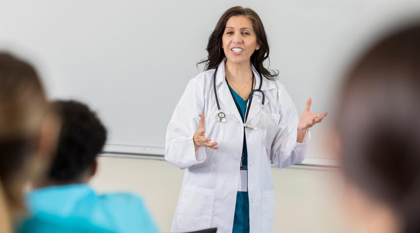 A doctor stands at the front of a classroom giving a lecture to medical students
