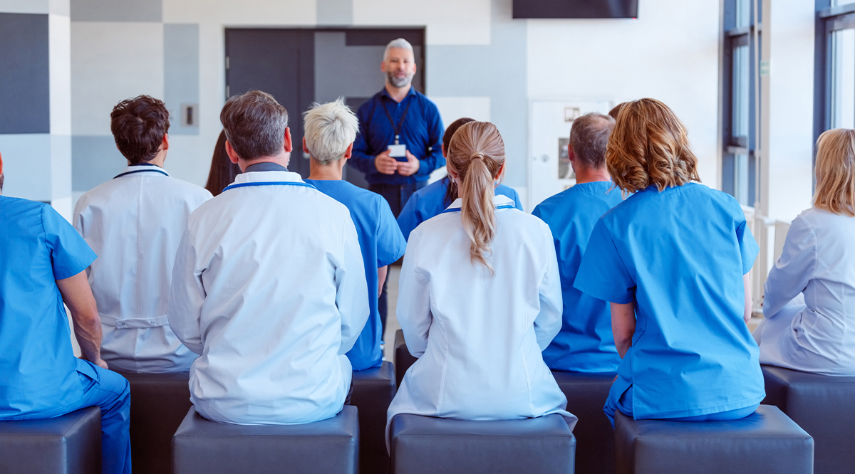 Group of doctors and nurses sitting in a conference room and listening to male speaker.