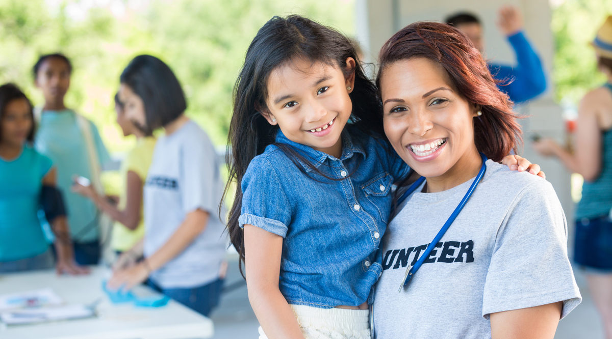 A smiling doctor holding a child patient at an outdoor health fair.