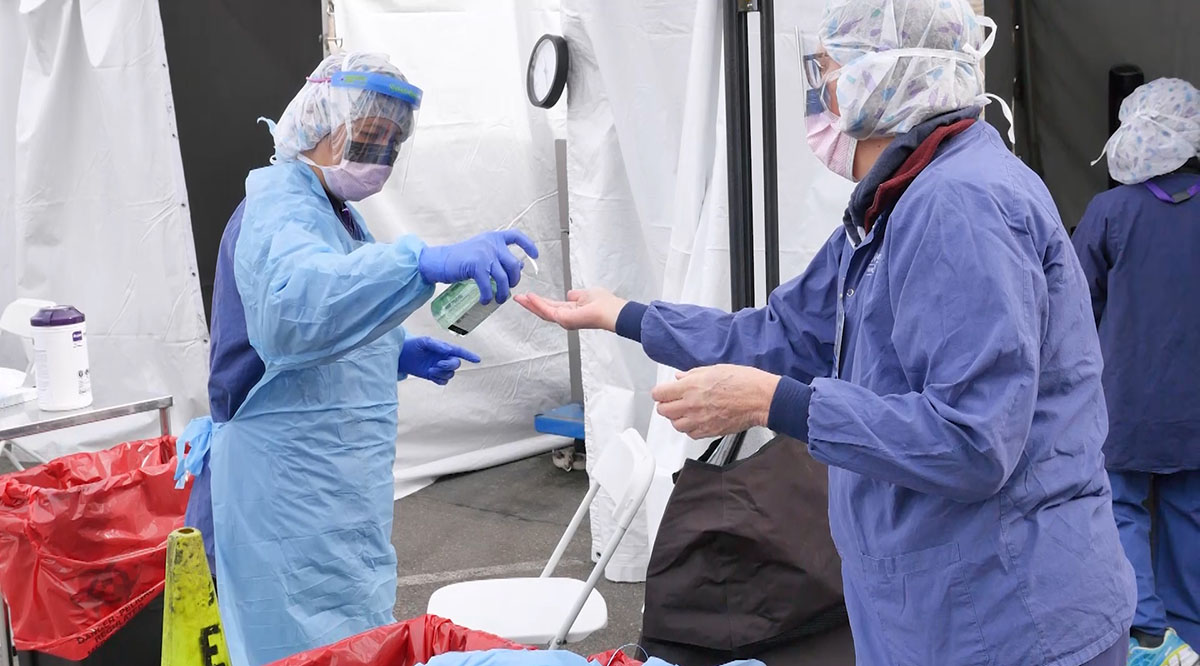 A UW Medicine nurse gets help sanitizing her hands after removing the gown and gloves she wore while screening a patient for COVID-19