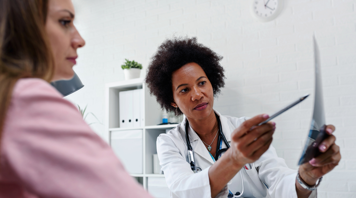 Female doctor talking with patient at desk in medical office.