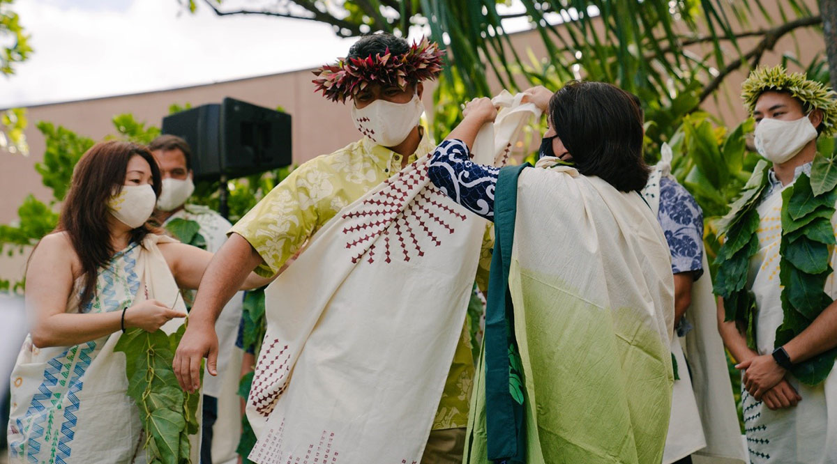 A student is flanked by two faculty members at the University of Hawaii at Manoa John A. Burns School of Medicine’s Kihei Ceremony, held the day before commencement. Each Native Hawaiian medical student makes their own kihei to tell the story of their journey to medical school.