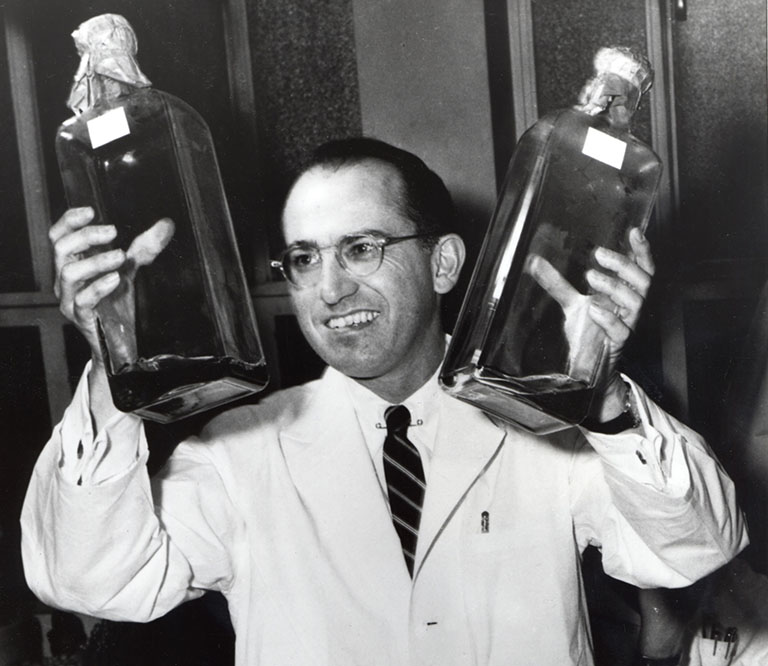 Jonas Salk holds two bottles of a culture used to grow polio vaccines in 1955