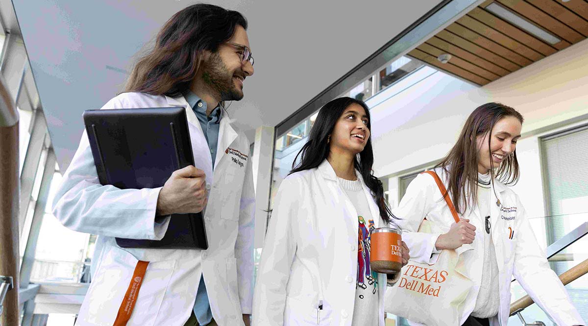 Three medical students -- two women and one man -- walk down a hallway while wearing white coats