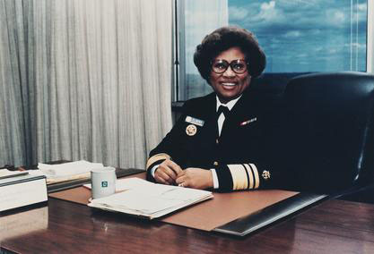 Joycelyn Elders sits at her desk smiling for the photograph while wearing her surgeon general uniform. 