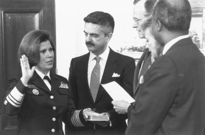 Antonia Novello takes an oath of office with her right hand raised and her left hand on a book. President George H. W. Bush is one of three other people also taking part in the ceremony. 