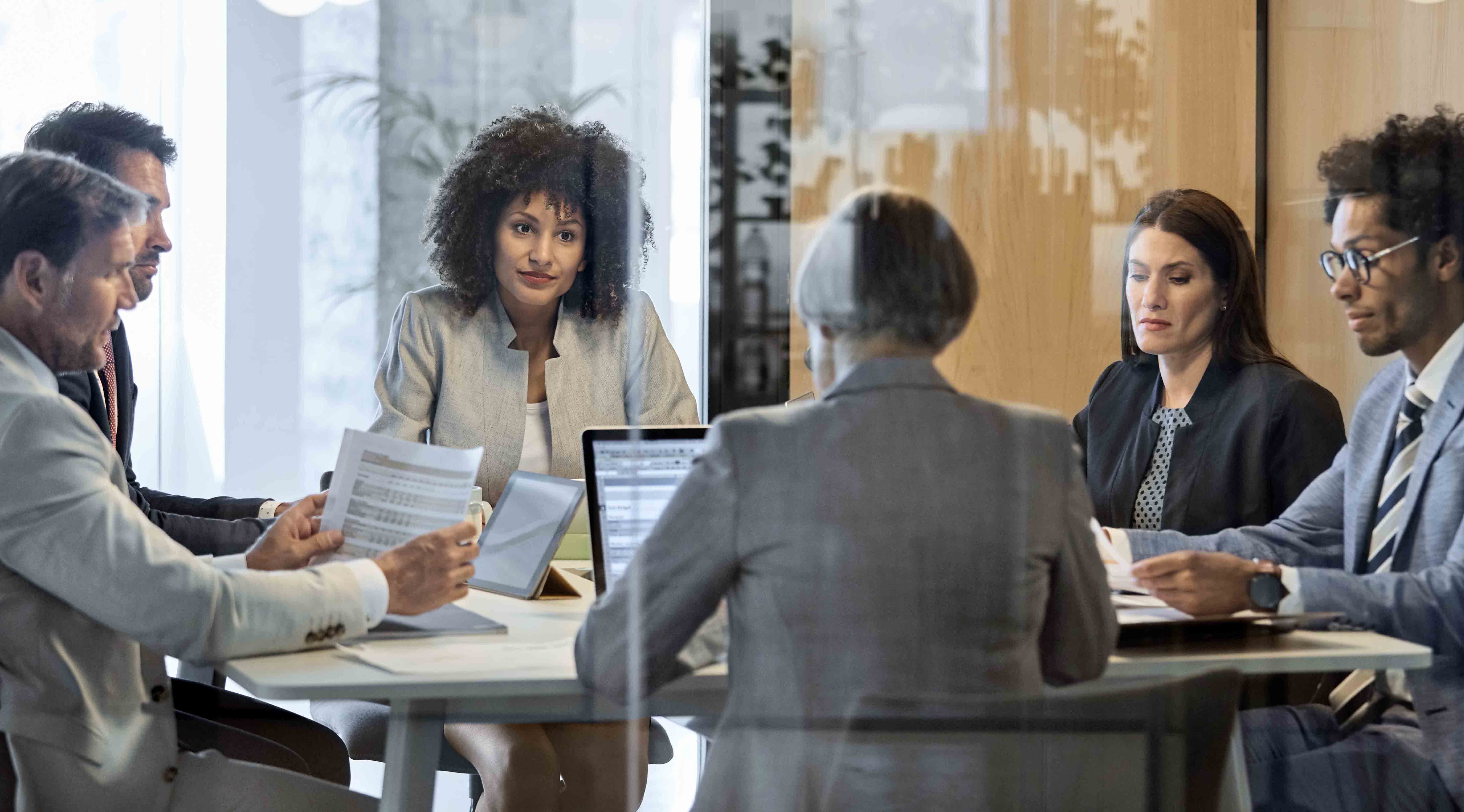 A group of people sit around a table in a meeting.