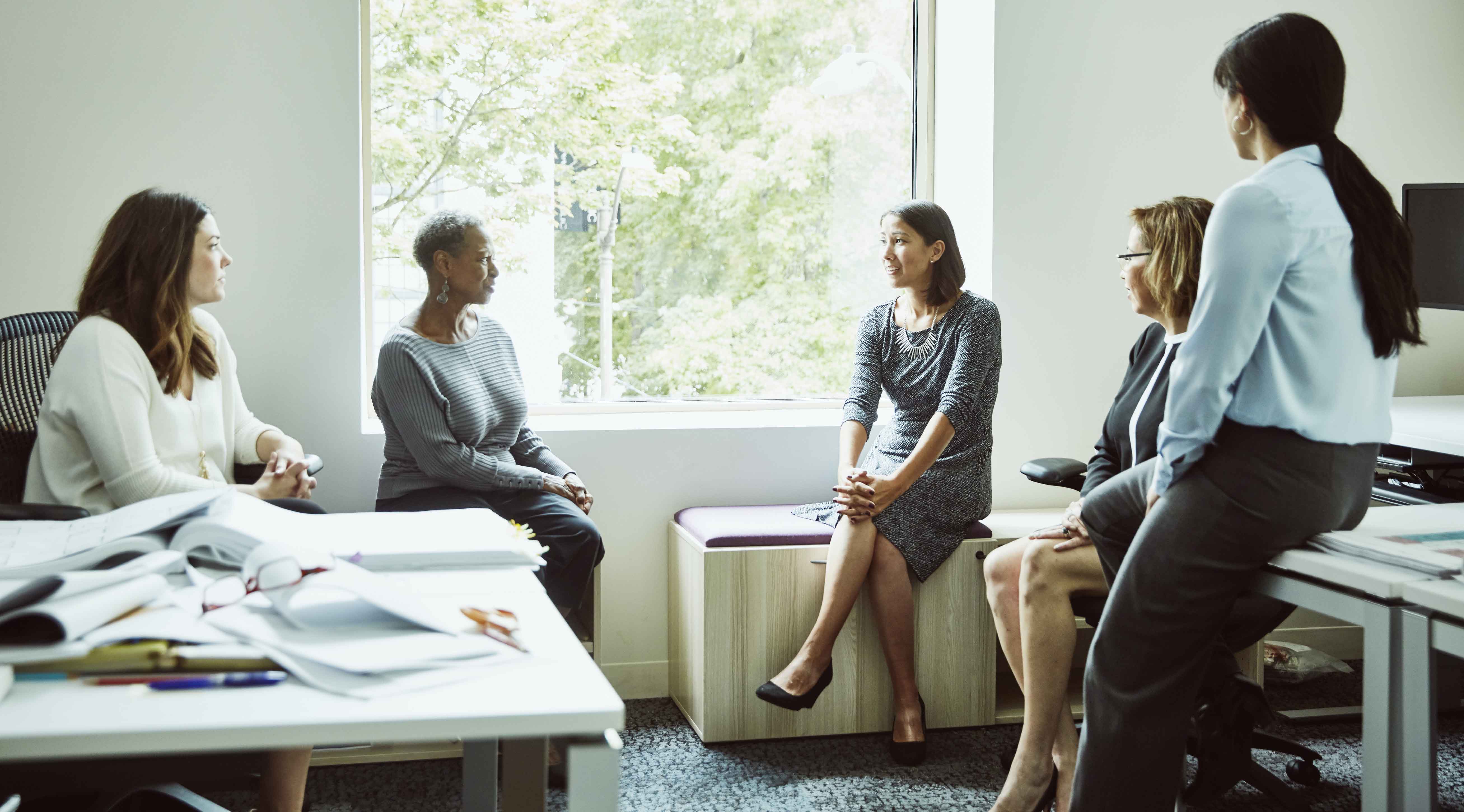 A group of women sit in a circle and discuss work. 