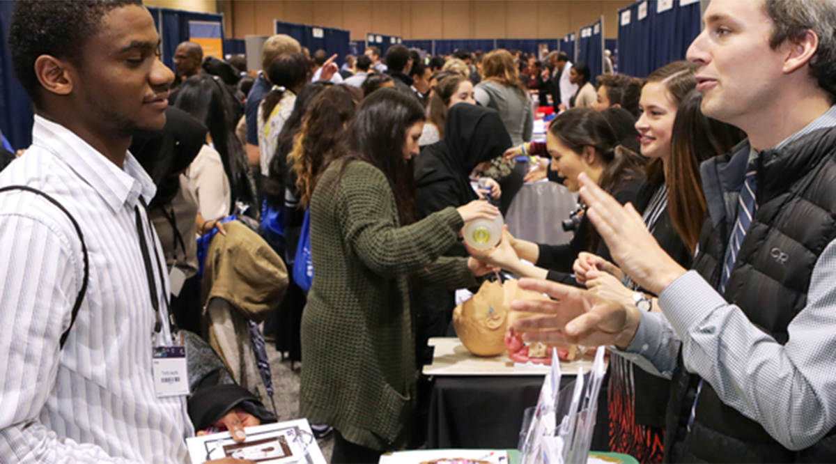 Two male students conversing during a medical career fair.