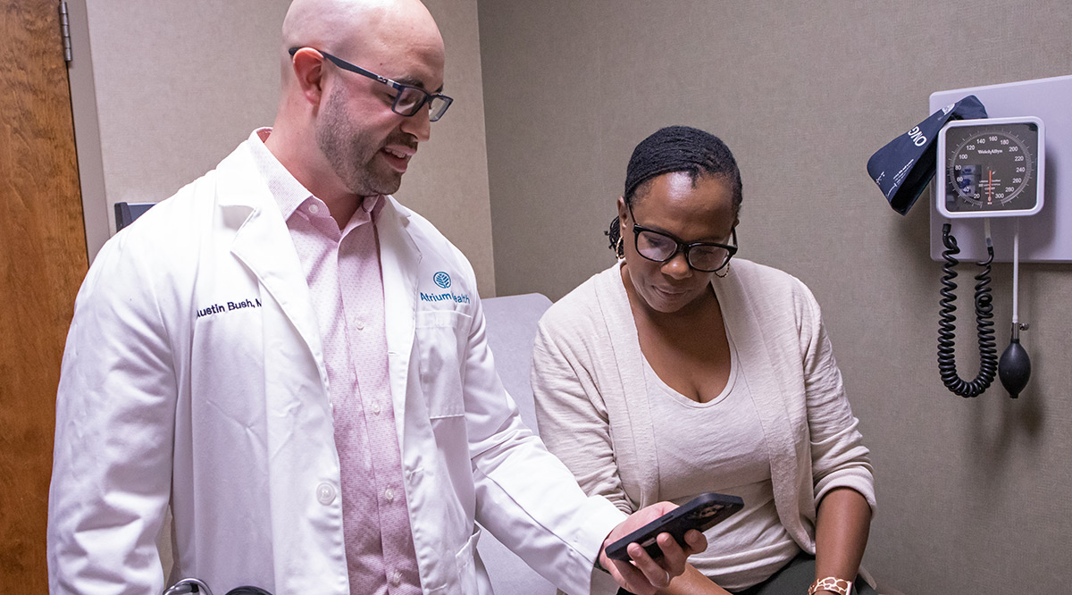 Austin Bush, MD, shows a patient at Atrium in North Carolina a tool on his phone. The tool records the doctor-patient encounter and produces notes for the doctor to review later.