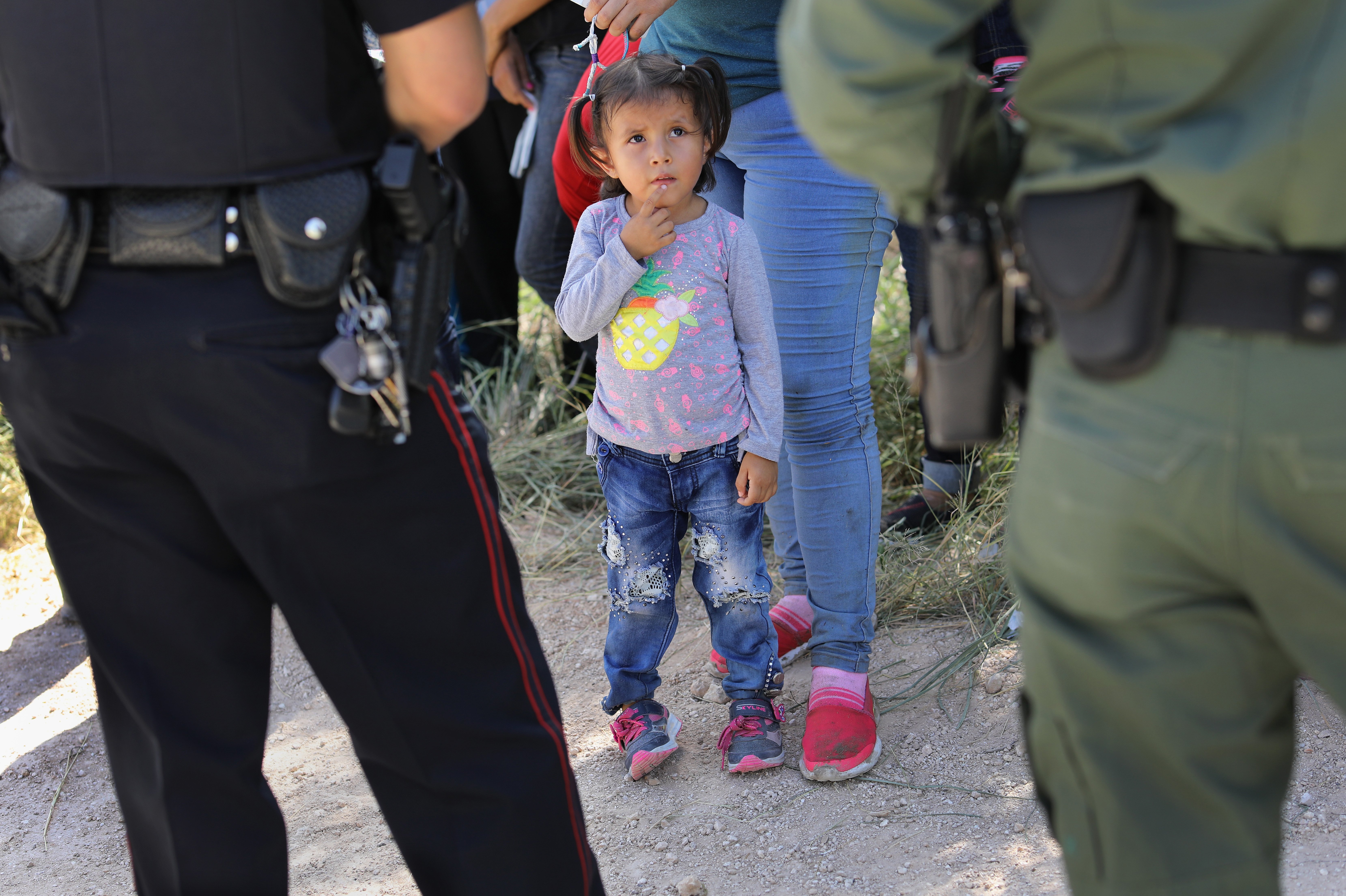 A Mission Police Dept. officer (L), and a U.S. Border Patrol agent watch over a group of Central American asylum seekers before taking them into custody on June 12, 2018, near McAllen, Texas. (Photo by John Moore/Getty Images) Child at border