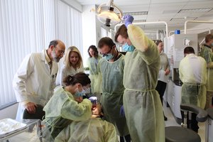 Three medical students and two professors surround a patient. One student examines the patient’s mouth while the others observe.