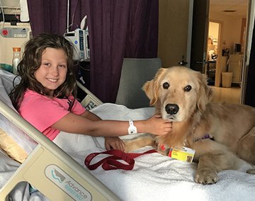 Smiling girl in hospital bed with dog next to her