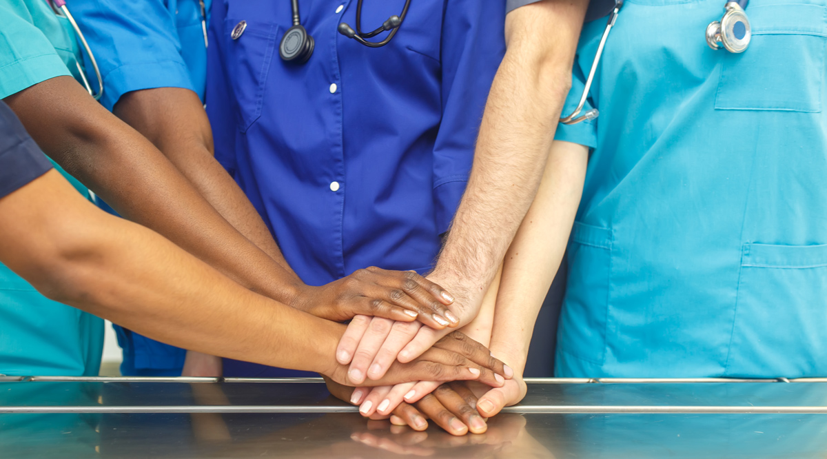 Diverse group of doctors stacking hands in an operating room table.