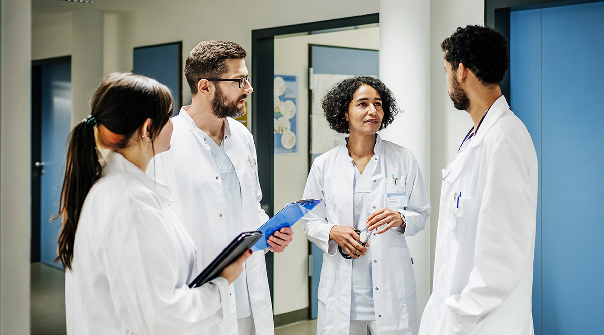 Four doctors in white coats having a discussion in a hospital hallway