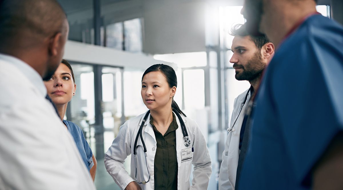 A group of five doctors stand in a circle having a conversation