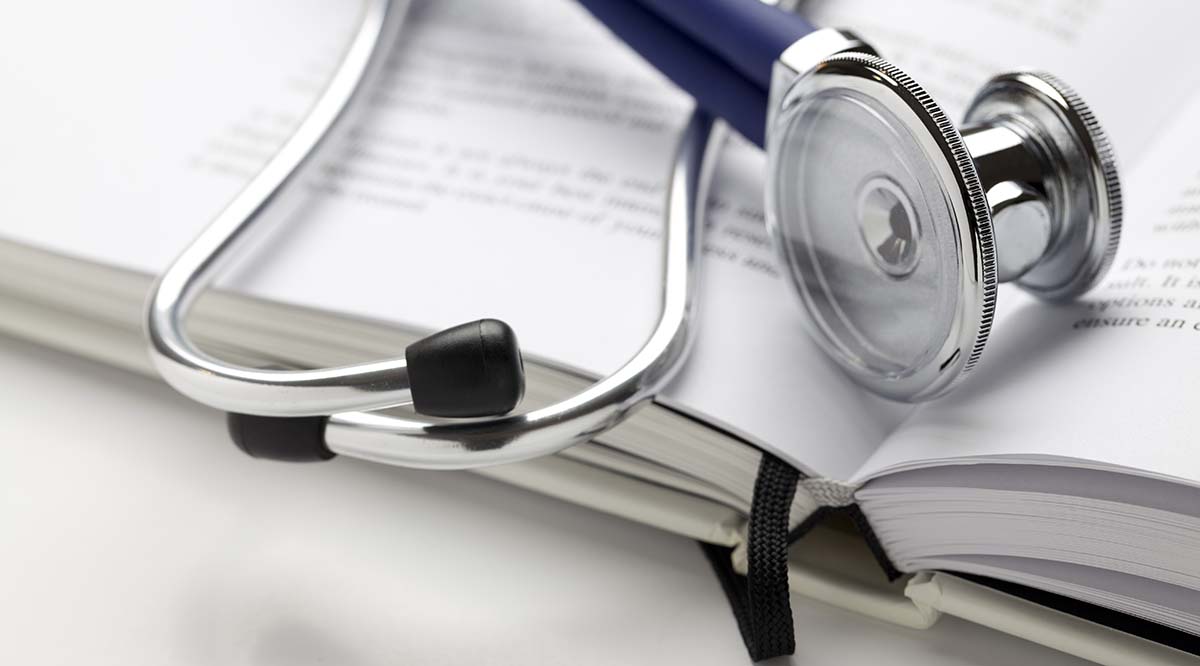 A metal stethoscope sits atop an open book