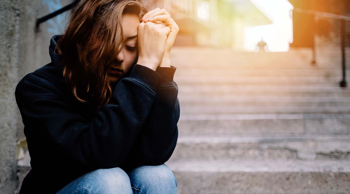 A young woman sitting on steps with her arms partially covering her face