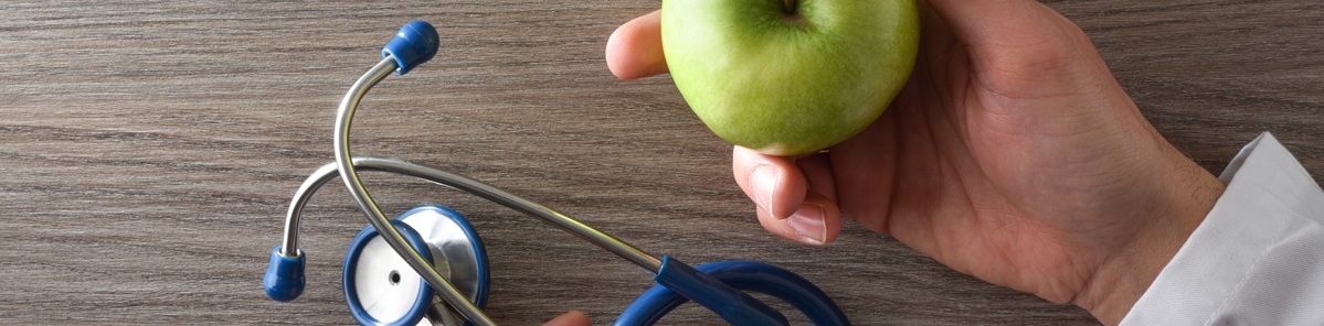 Nutritionist doctor with apple and stethoscope in hands on table