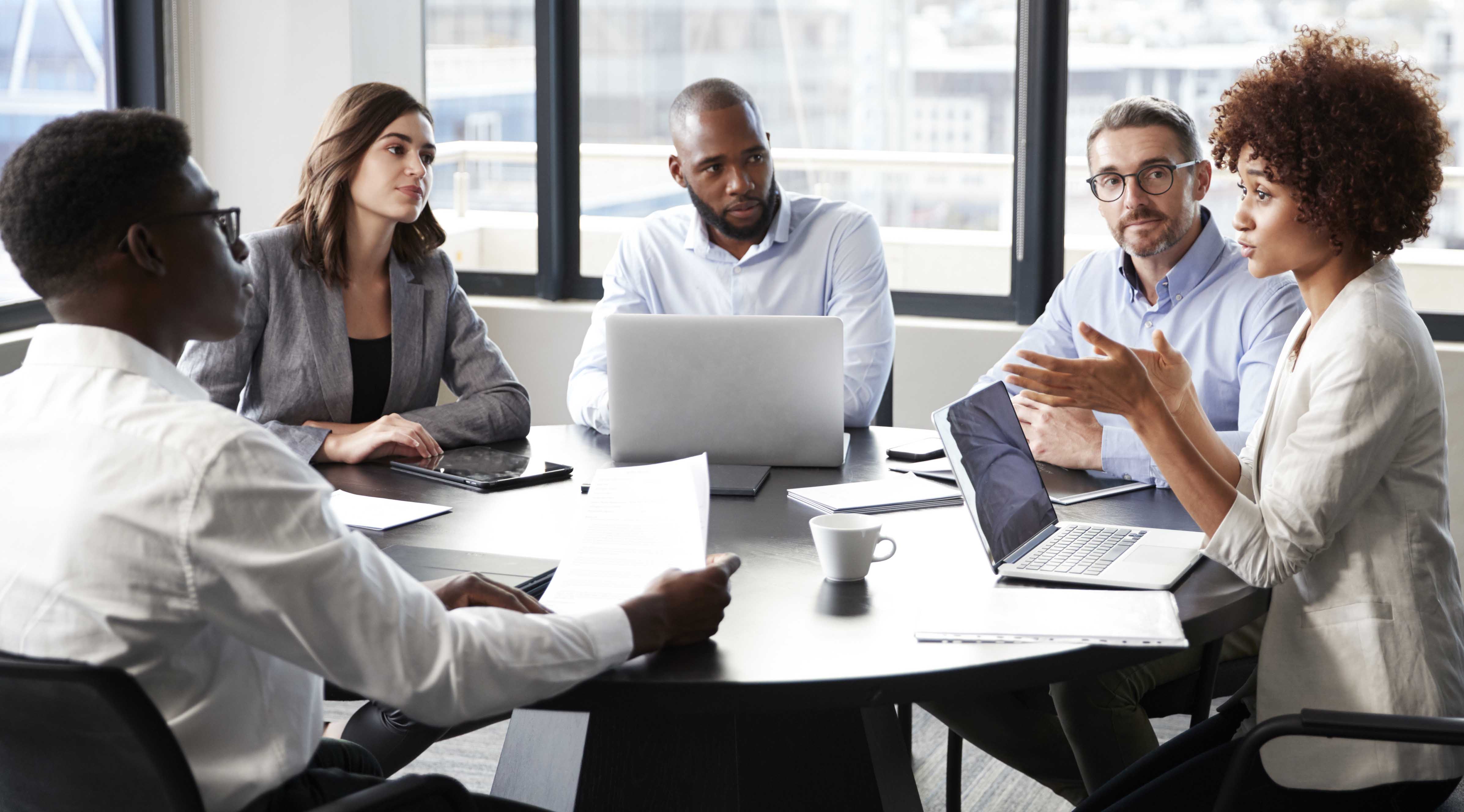 A diverse group of people have a discussion around a table. 