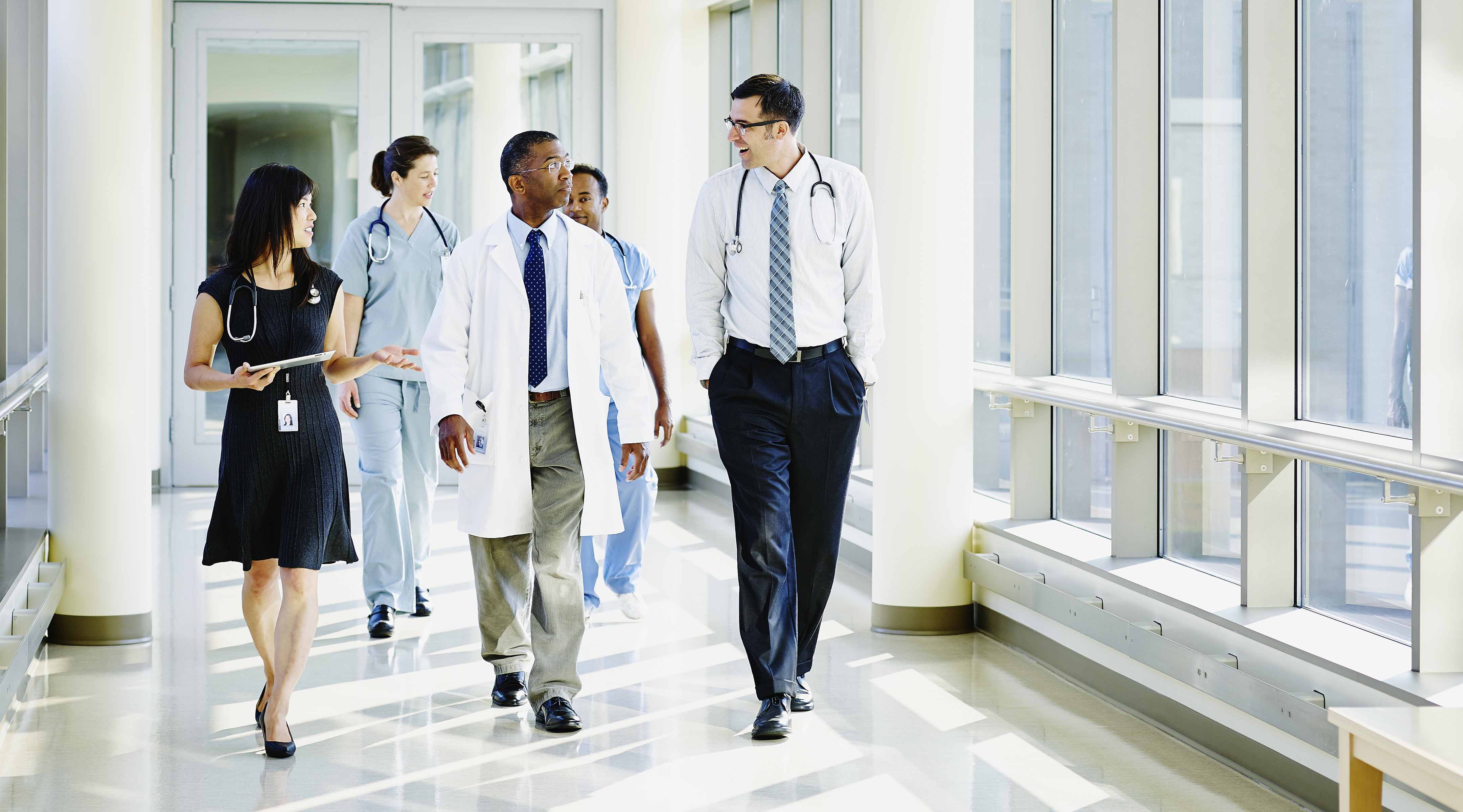 Leading Organizations A group of doctors have a conversation while walking down a hallway.