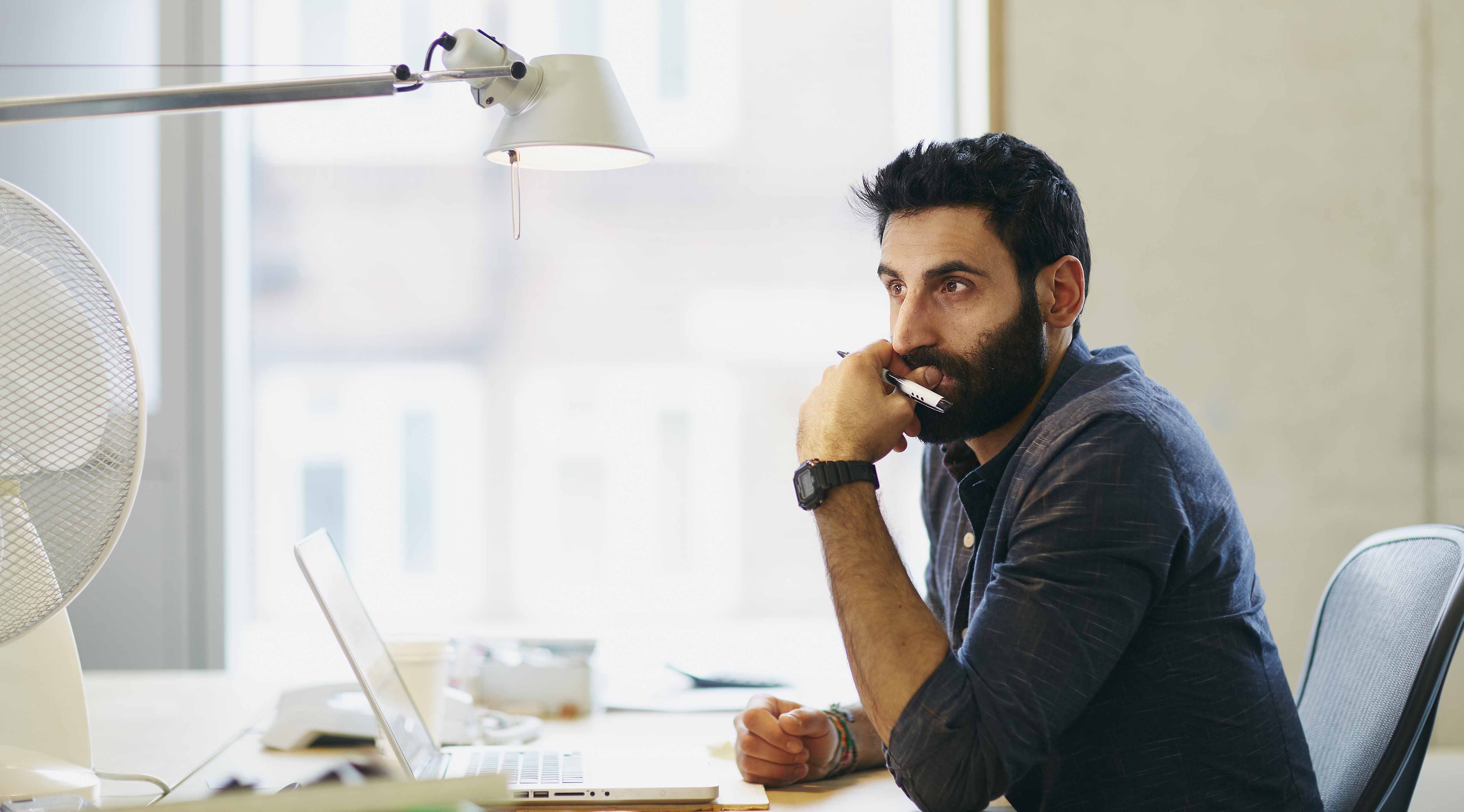 A man sits and contemplates at a laptop computer