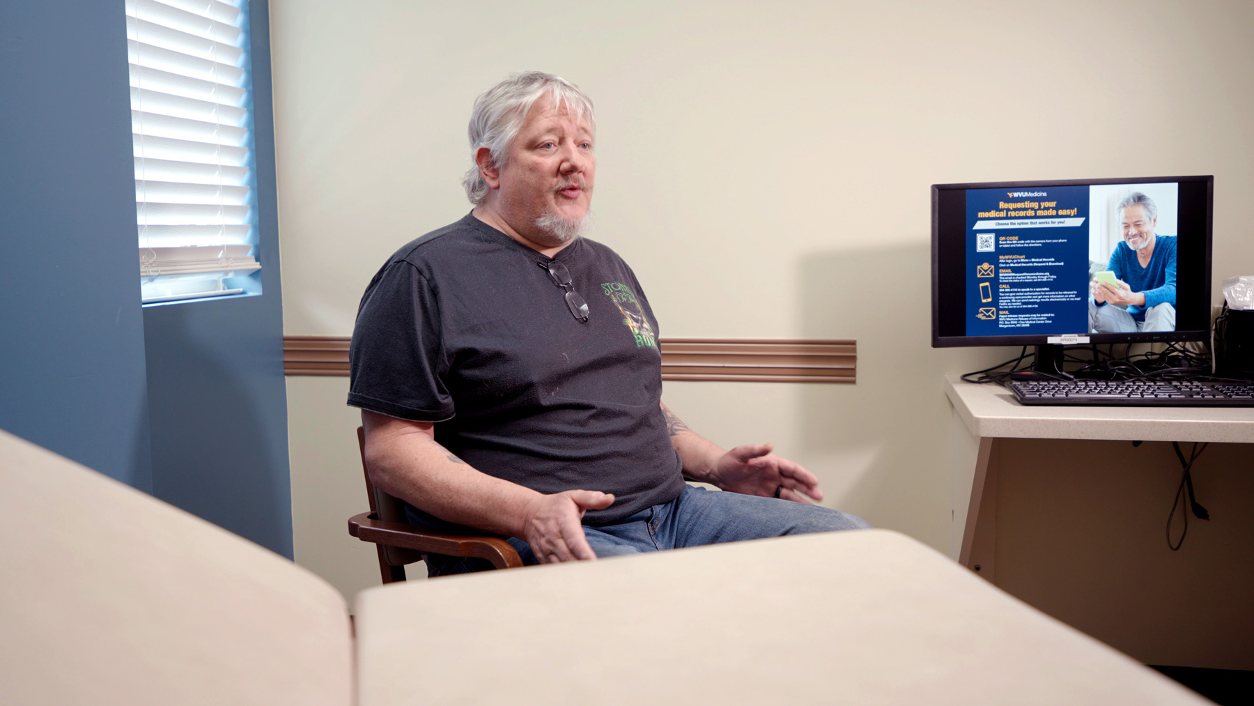Scott Heffner sits in a patient room. There is a laptop on the counter beside him.