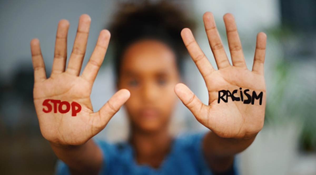 African american girl standing indoors and looking at the camera. She's showing a message that says Stop Racism on her hands.