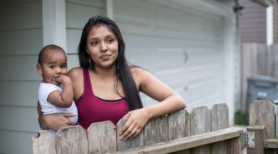 Young Native American mom holds baby at front gate to their home