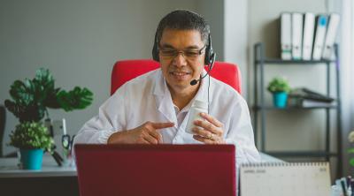 A doctor wearing headphones looks at a laptop screen