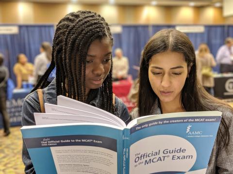 Two young women read the same Official Guide to the MCAT Exam prep book