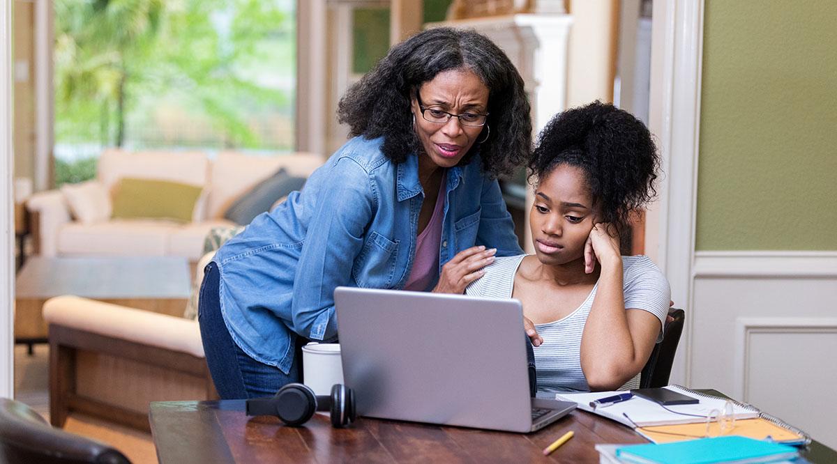 A mother looks at a computer screen with her daughter who looks upset