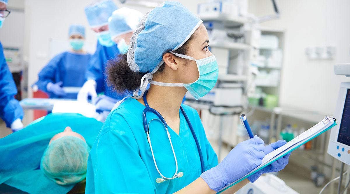 A nurse in hospital scrubs looks up from her checklist