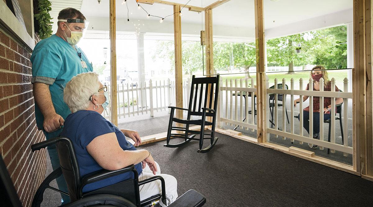 An elderly woman at a nursing home entertains a visitor while maintaining precautions against COVID-19