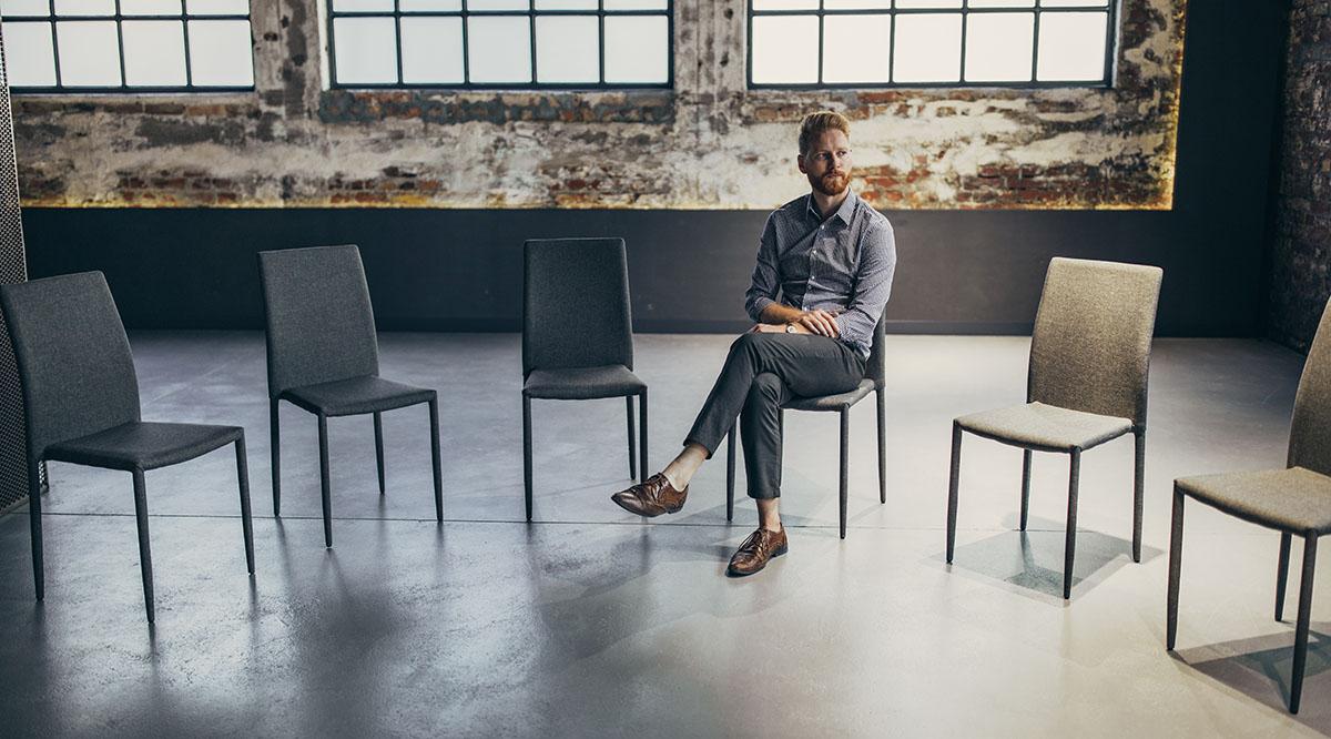 A man sits alone in a circle of chairs