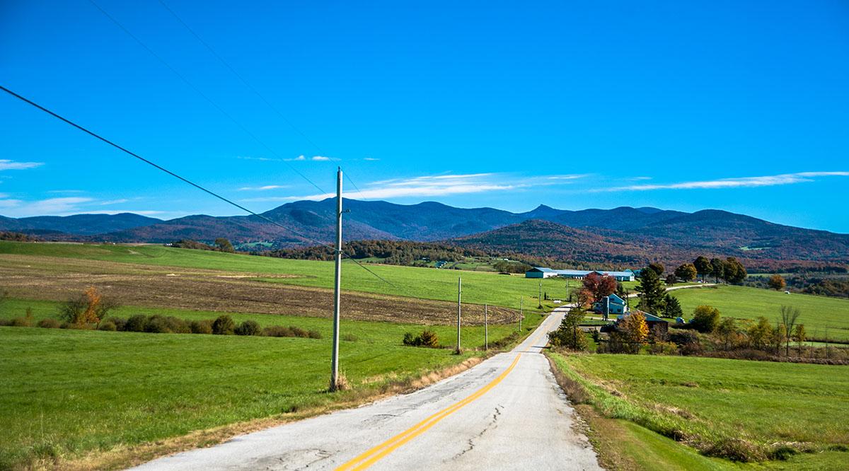 A road leads through a green field toward a hill