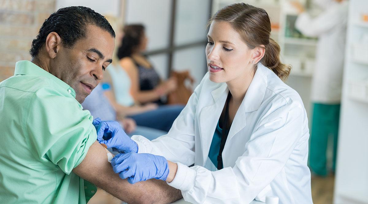 A woman doctor puts a bandage on a patient after giving him a vaccine