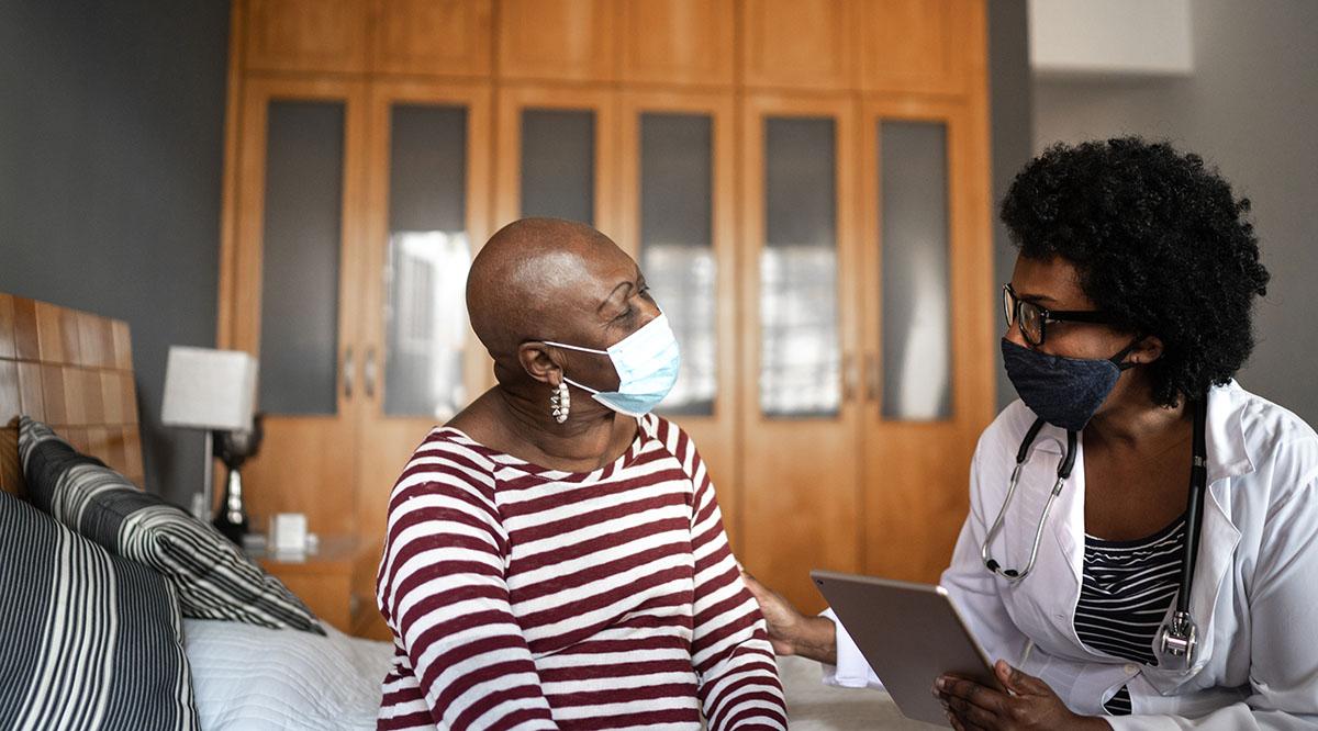 A doctor speaks to an older woman in a mask