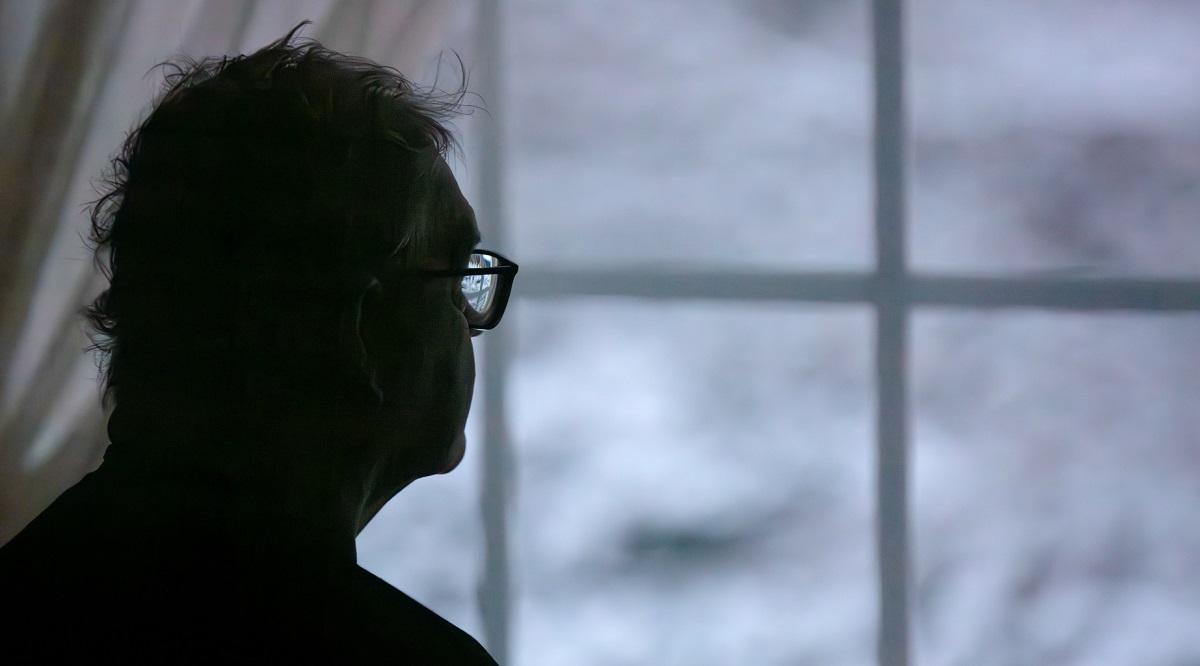 Lonely senior man looking out of window at winter 
