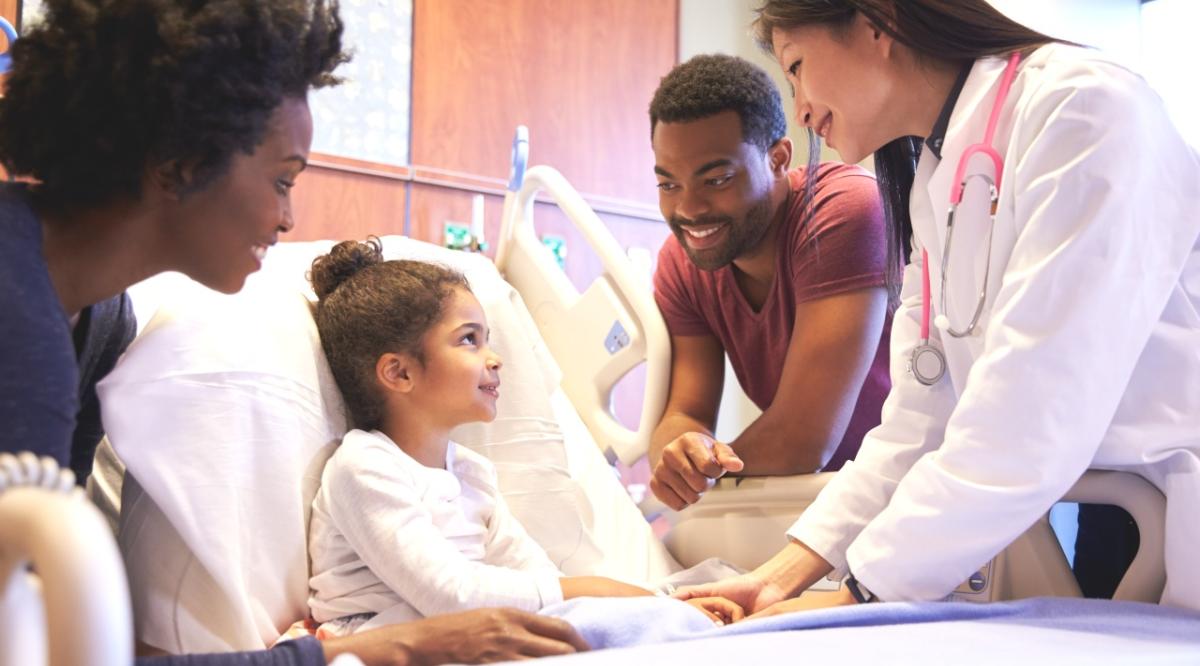 child in hospital bed smiling with parents and doctor
