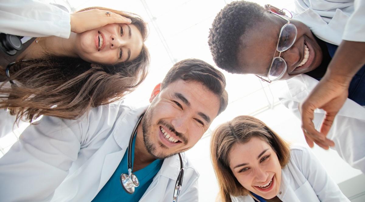 Group of people of 4 medical workers who are bending over looking down and laughing merrily