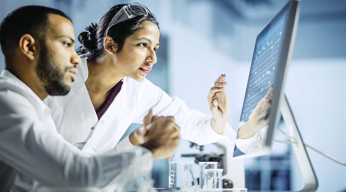 A male researcher and a female researcher look at a flat screen computer monitor