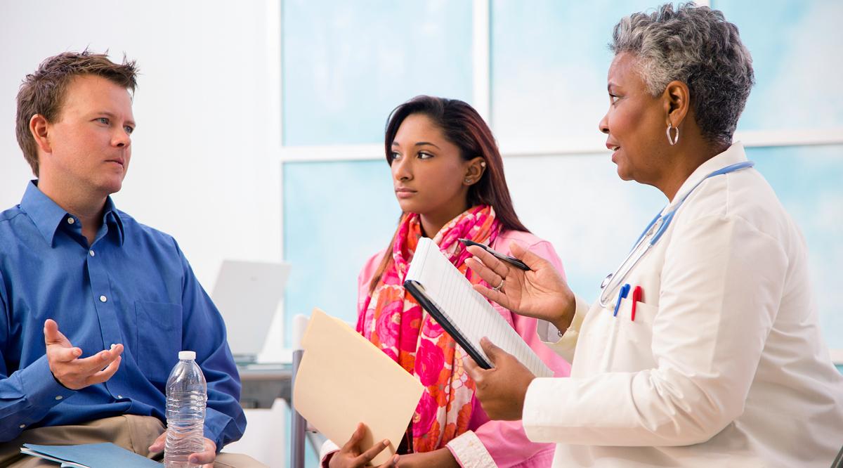 A female doctor talking with man and woman patients in an office or clinic.