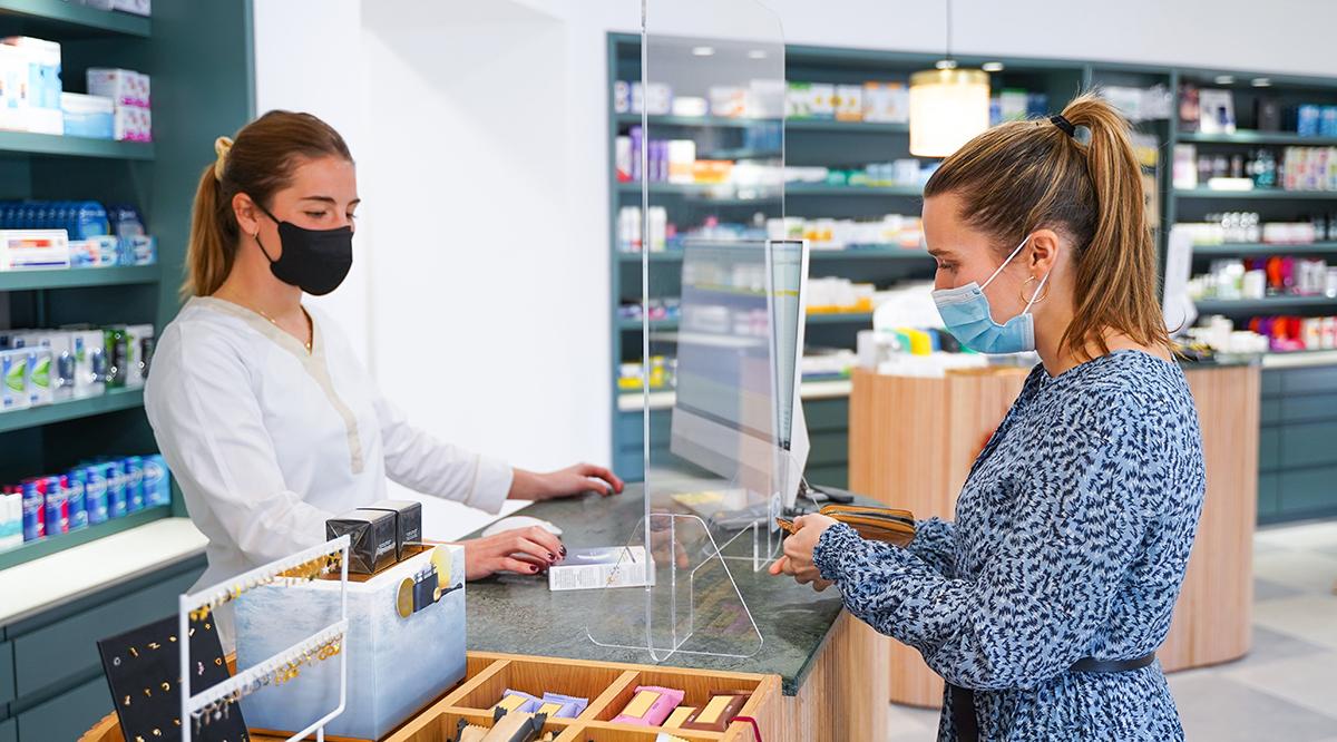 Pharmacist with ffp2 mask charging the client with a surgical mask