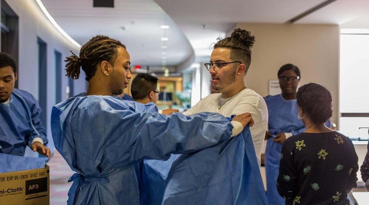 one medical professional assists another with putting arms through a surgical gown