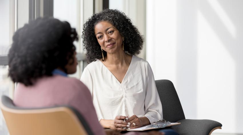 A mental health counselor meets with her patient in a sunlit room