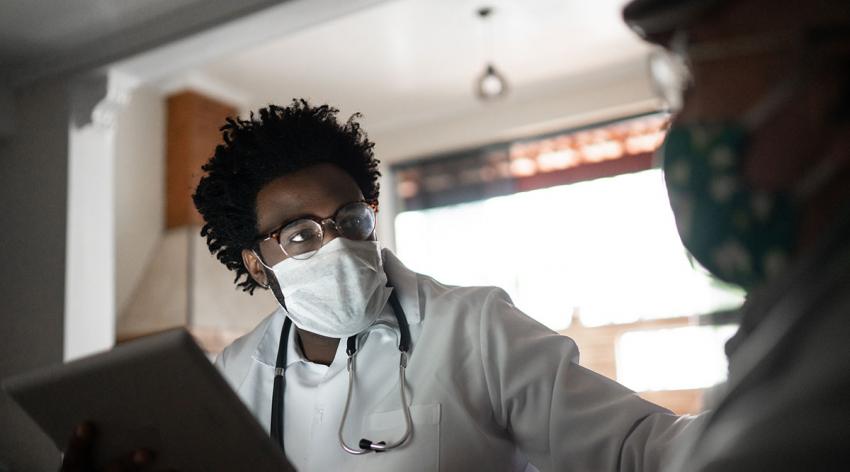 A Black physician in a mask talks to a patient in a mask