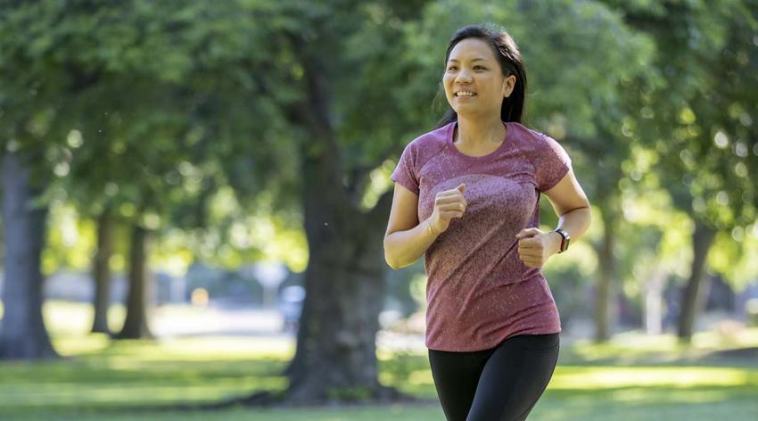 Christina Kashiwada runs through a park area with trees in the background