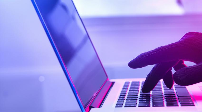 A gloved hand types on the keyboard of a laptop