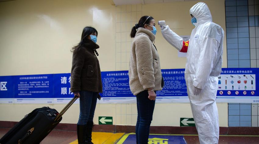 A person in a biohazard suit takes a person's temperature